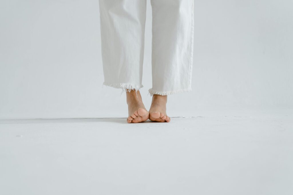 Close-up of bare feet in white jeans on a white minimalist background.