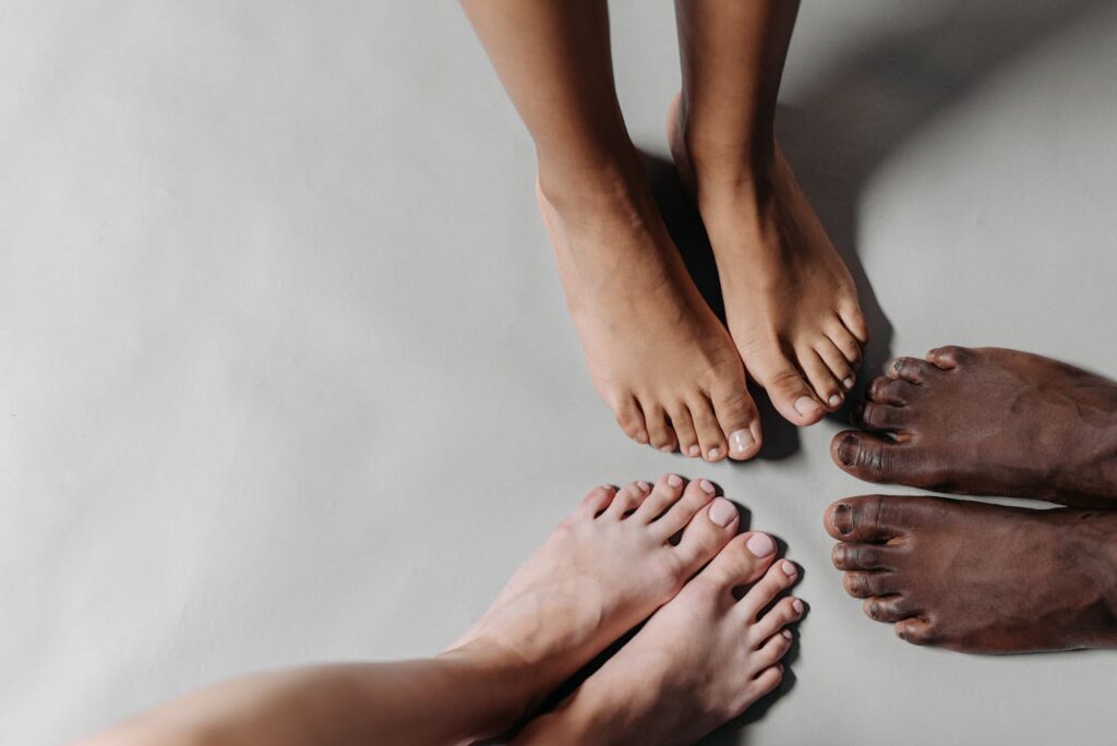 Close-up of three diverse pairs of barefooted feet standing on a white surface.