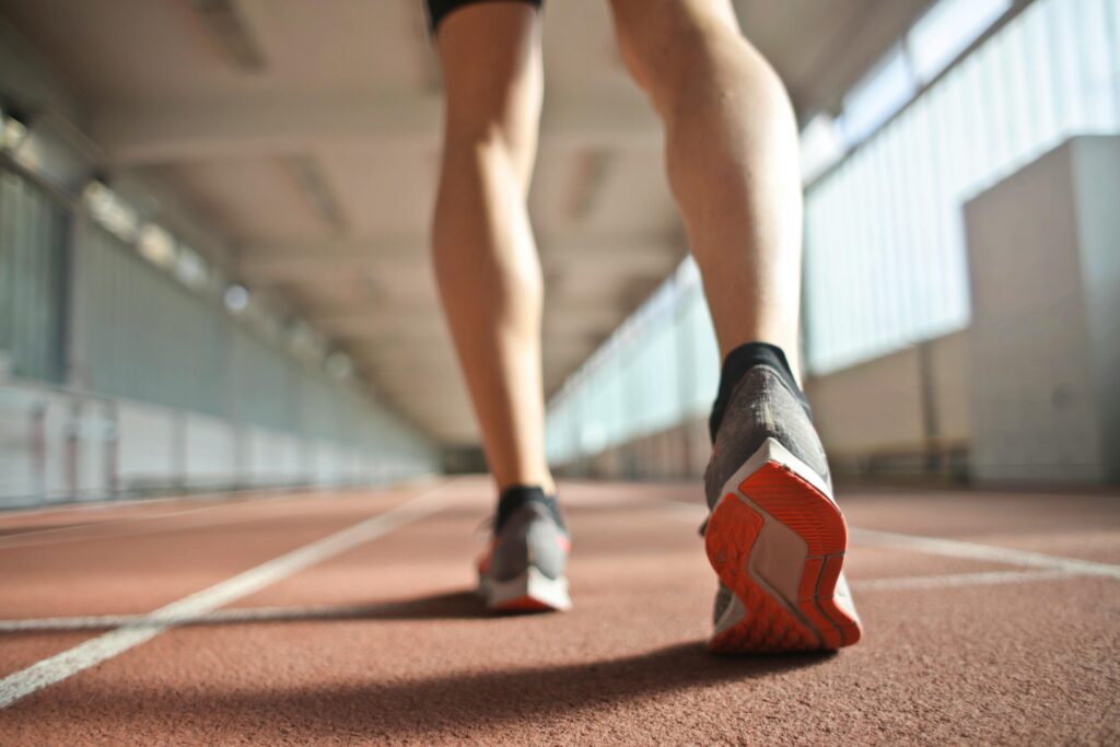 From below back view of crop athlete in sports shoes standing on running track while preparing for start during training