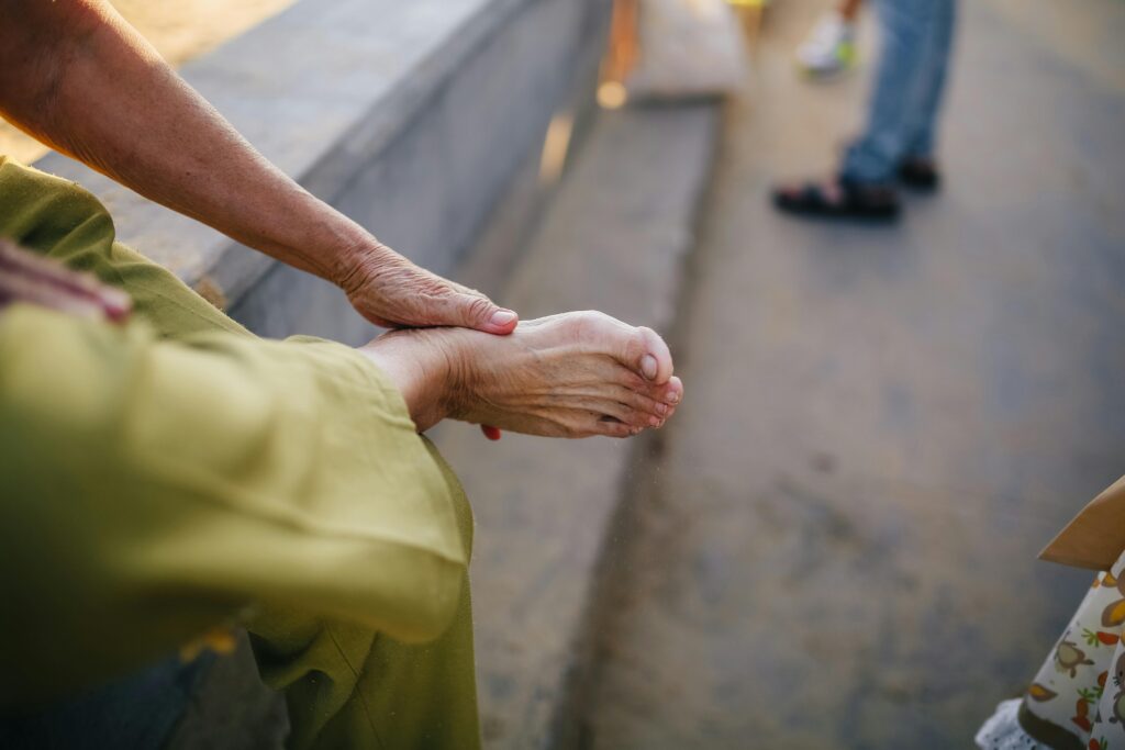 An elderly person sitting outdoors massaging their foot for relief.